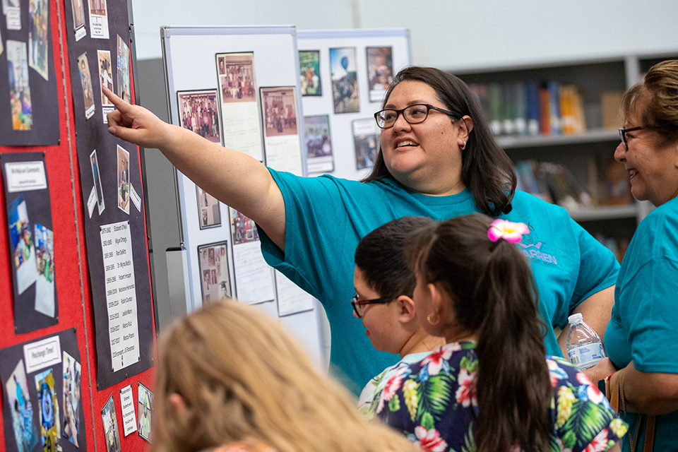 A woman in glasses points up at a photo pinned on a board
