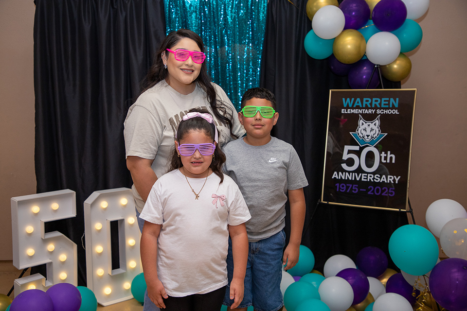 A mom and her son and daughter pose with colorful glasses on