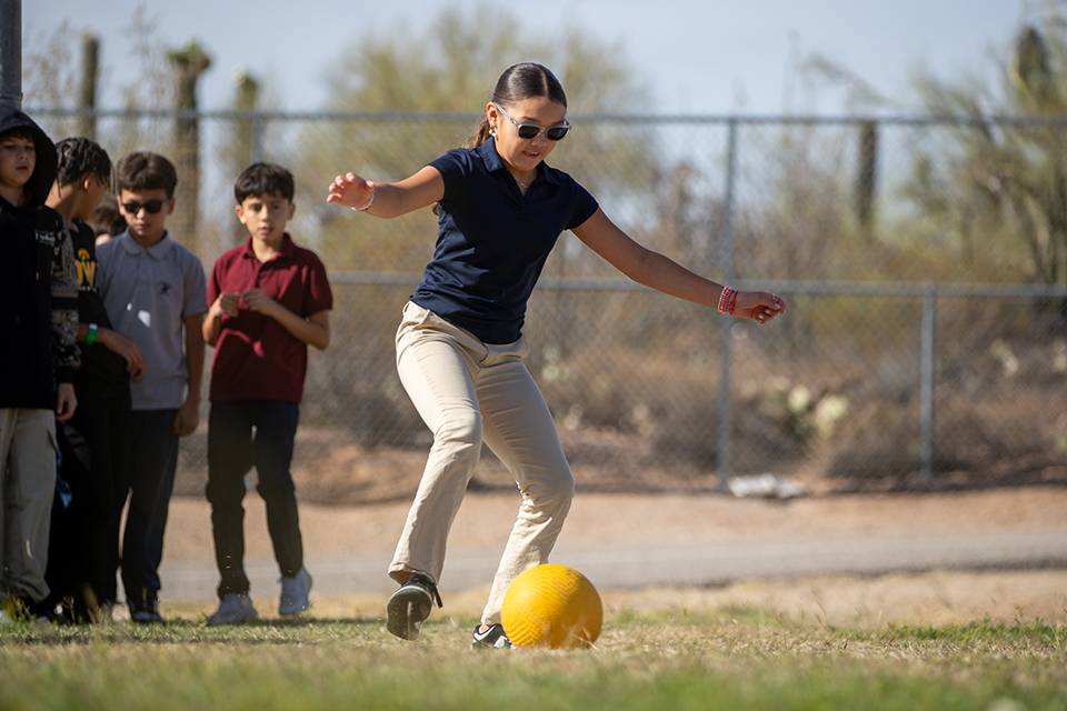 A girl kicks a yellow ball across the field