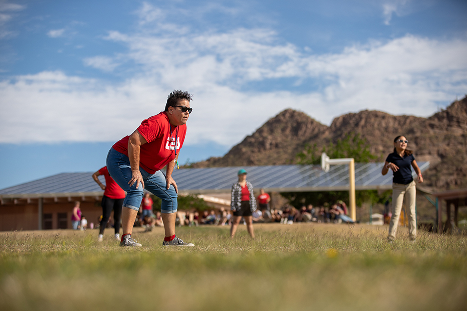 A teacher puts her hands on her legs as she watches the ball