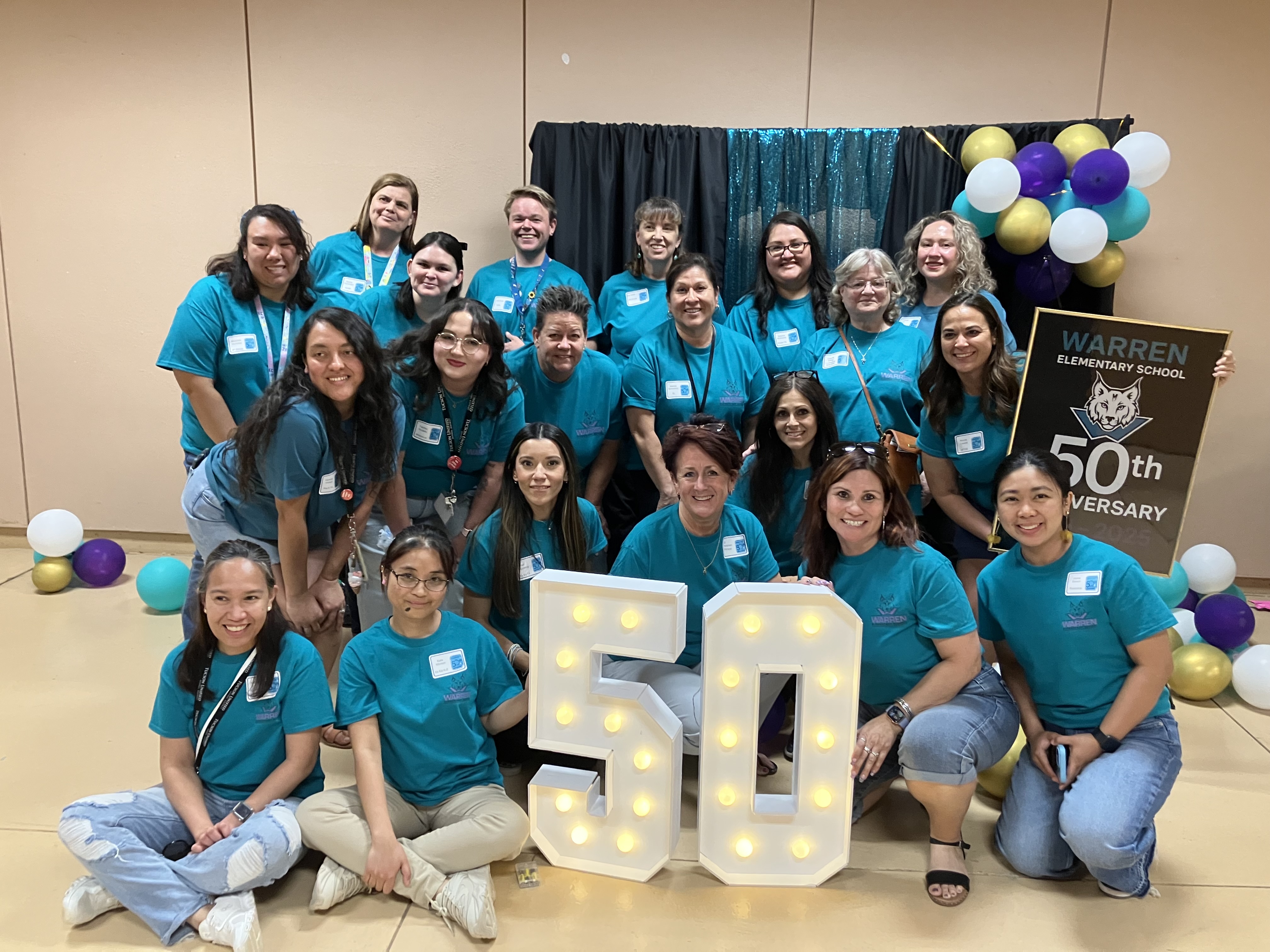 A group of people in blue shirts around a light up 50 sign