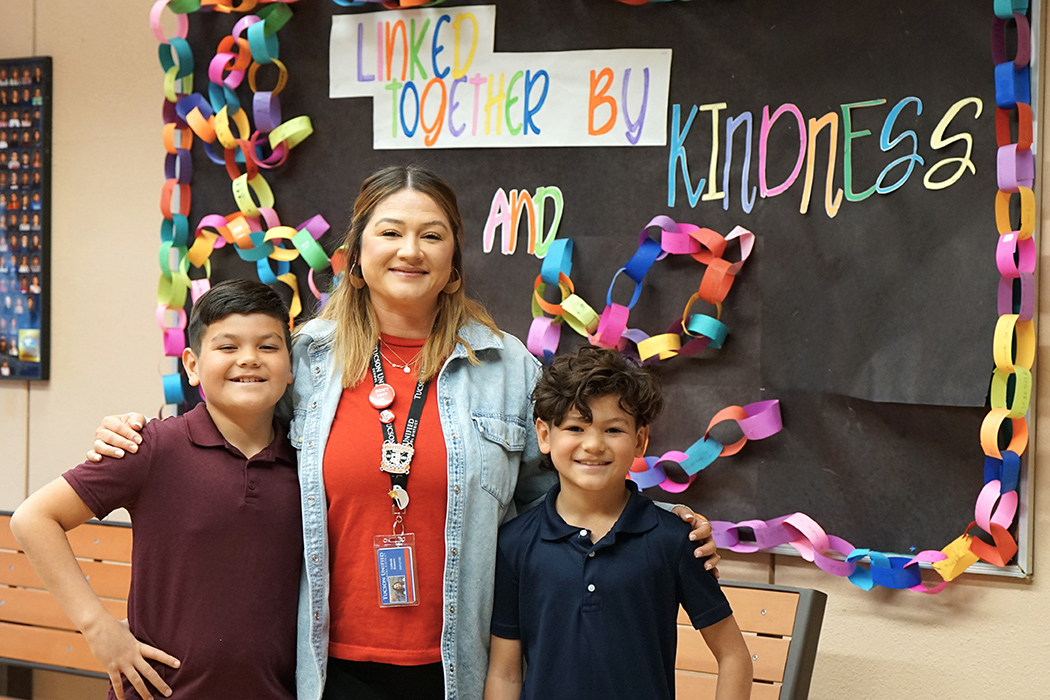 A woman stands with her two young sons in her classroom